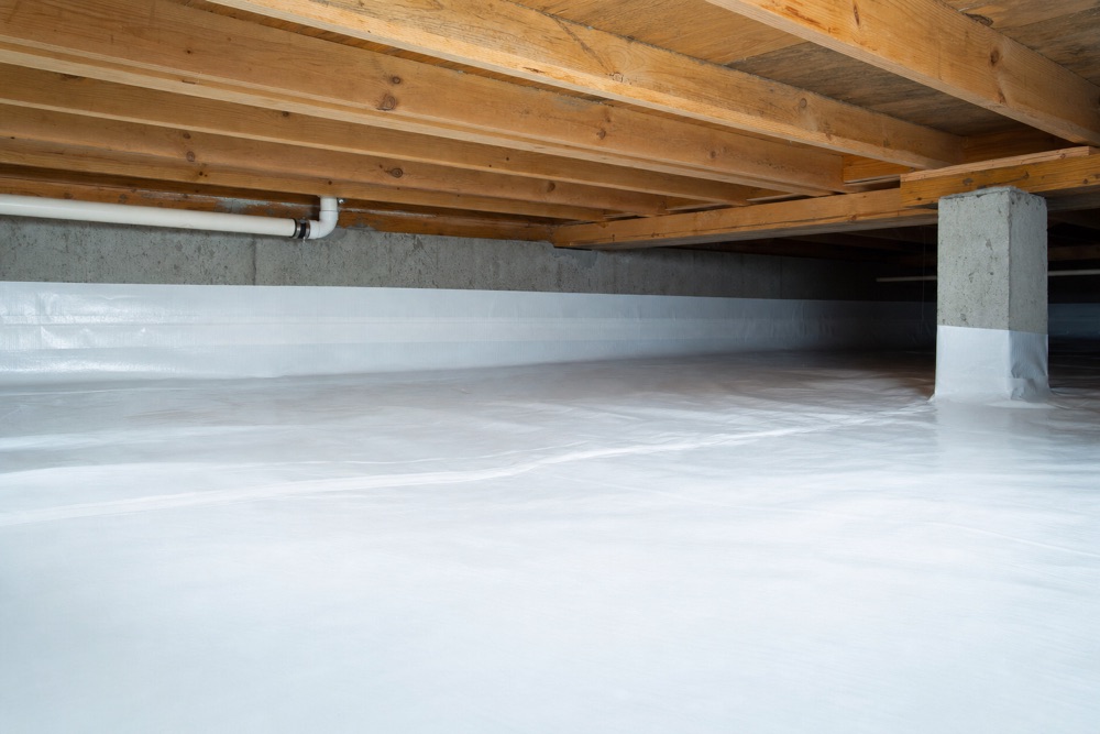 Crawlspace under a Fraser Valley home with a sealed white vapour barrier covering the ground below the floor joists